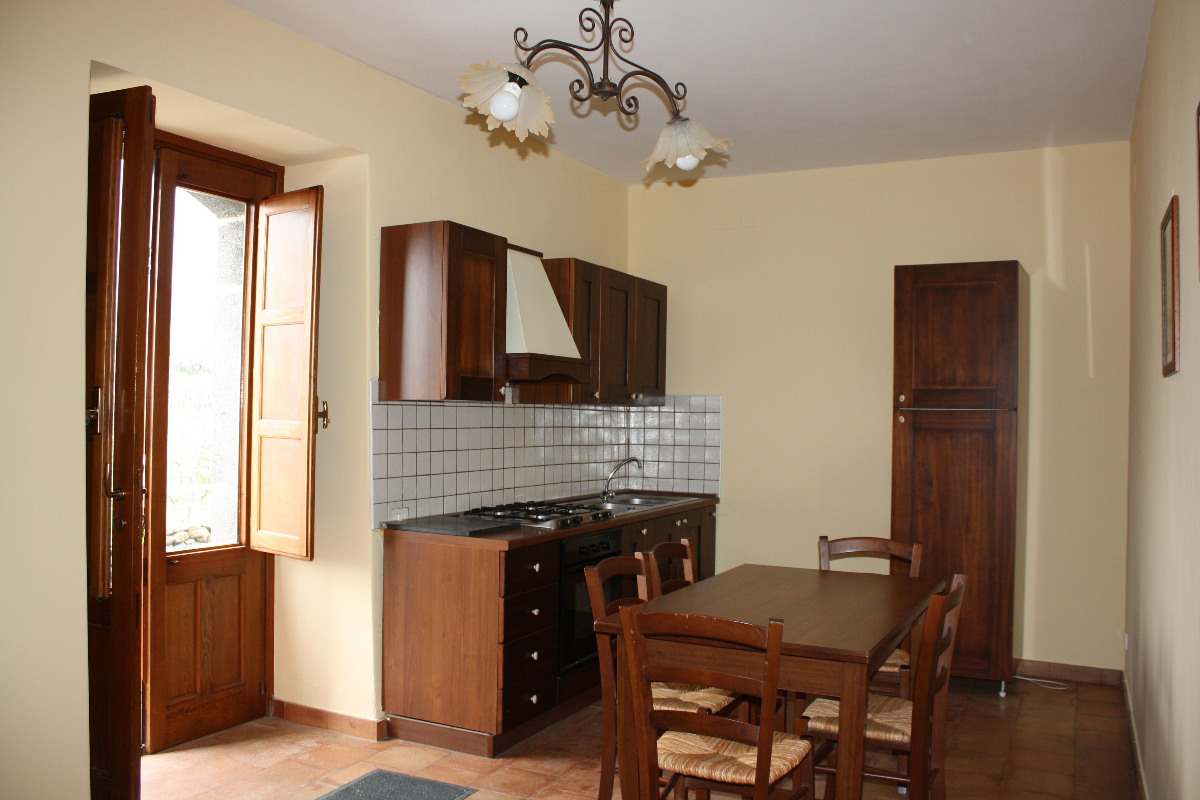 Una cocina con armarios de madera, un respuesto de azulejos, una estufa y una mesa de comedor con sillas.