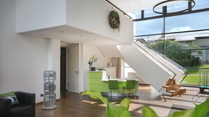 A modern interior with a staircase leading to a balcony, a reception desk, and a seating area with a plant. - GolfHotel Gut Neuenhof (Fröndenberg/Ruhr)