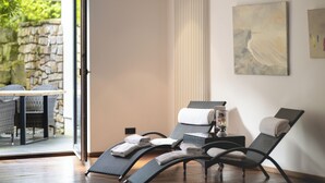 A sun lounger and a chair in a room with a stone wall and a glass door leading to an outdoor area. - GolfHotel Gut Neuenhof (Fröndenberg/Ruhr)