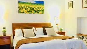 A hotel room with a large bed, a nightstand, a bedside table with a lamp, and a painting of a sunflower field on the wall. - Hotel Garibaldi (Frosinone)