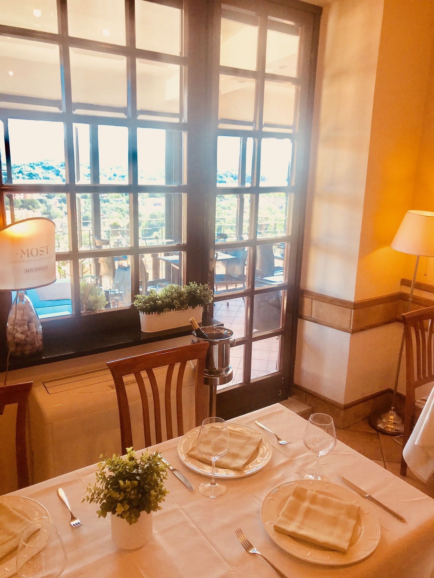 A dining table set with plates, glasses, and cutlery, a candle, and a window with a view of the outdoors.