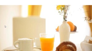 A breakfast setting with a cup, a glass of orange juice, a croissant, and a vase with flowers. - Hotel Garibaldi (Frosinone)