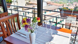 A dining table set with a vase of flowers, wine glasses, and cutlery on a balcony with a city view. - Hotel Garibaldi (Frosinone)