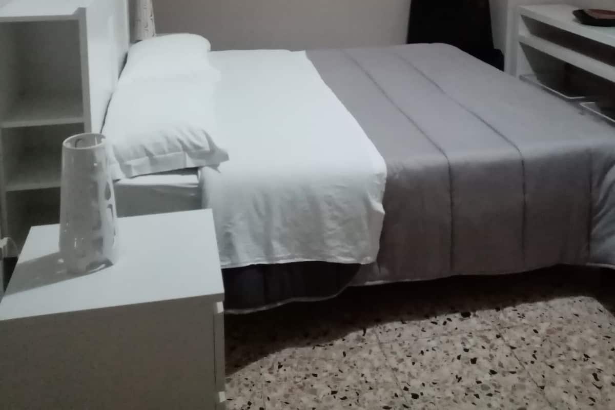 A bedroom with a bed, a desk, a chair, and a small table with a lamp.