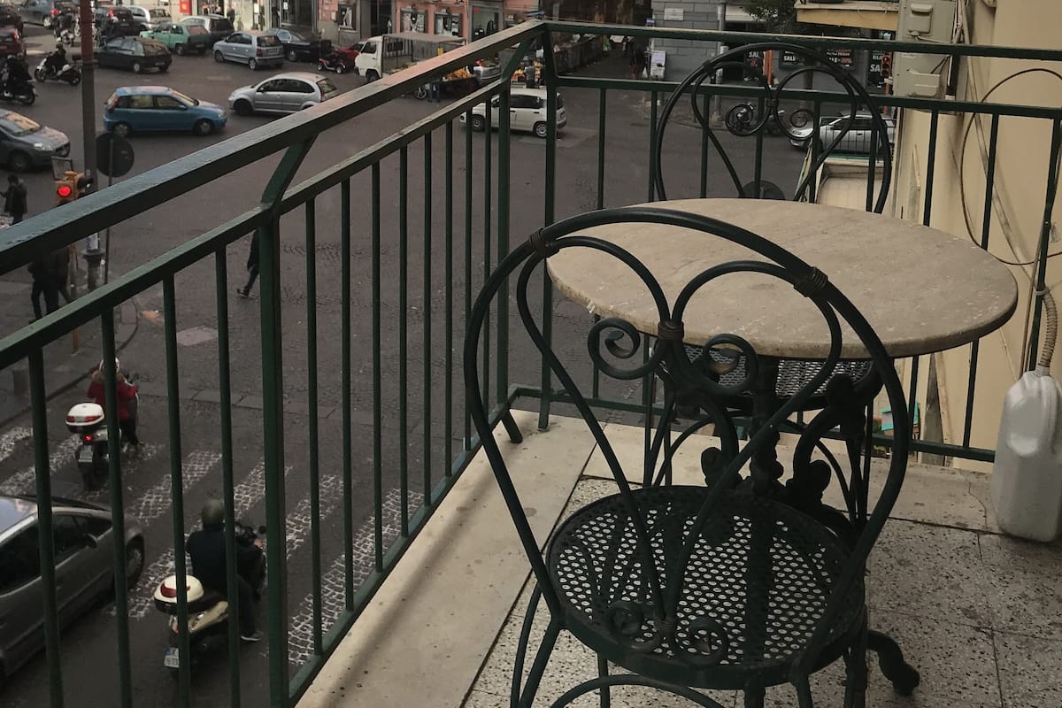A balcony with outdoor seating, overlooking a busy street with cars and pedestrians.
