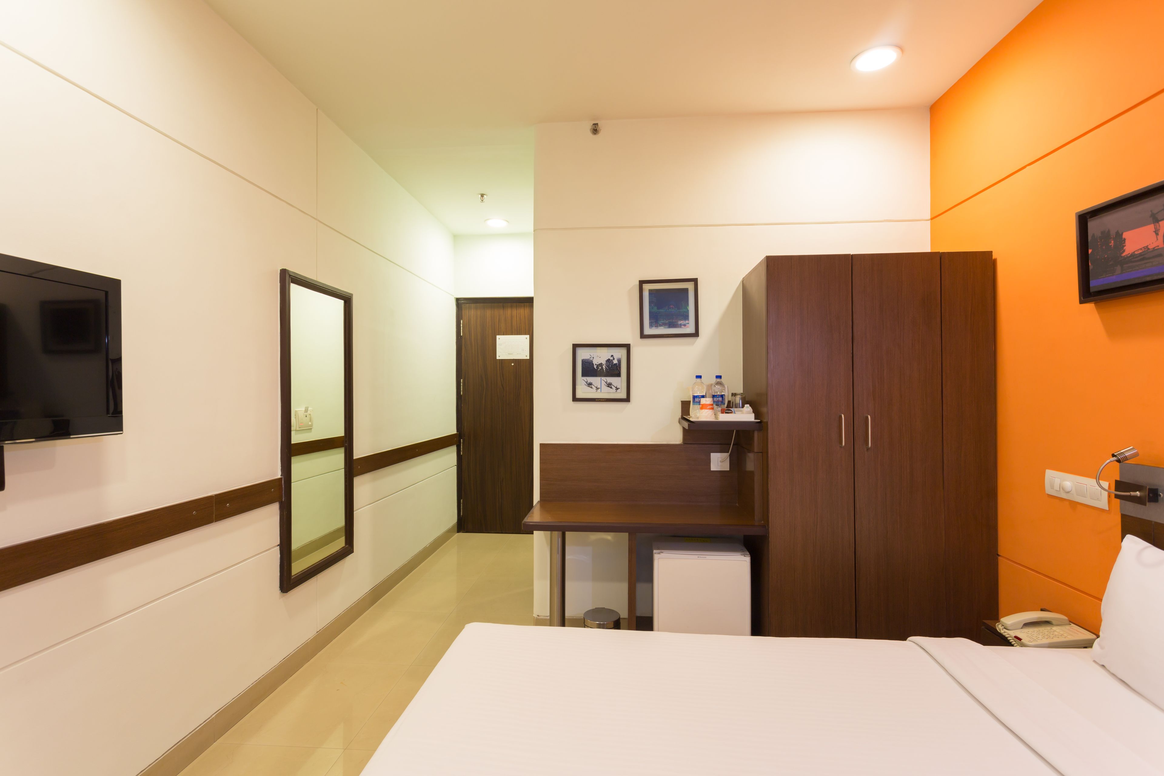 A hotel room with a bed, a desk, a television, a wardrobe, and a small refrigerator.