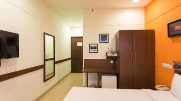 A hotel room with a bed, a desk, a television, a wardrobe, and a small refrigerator.
