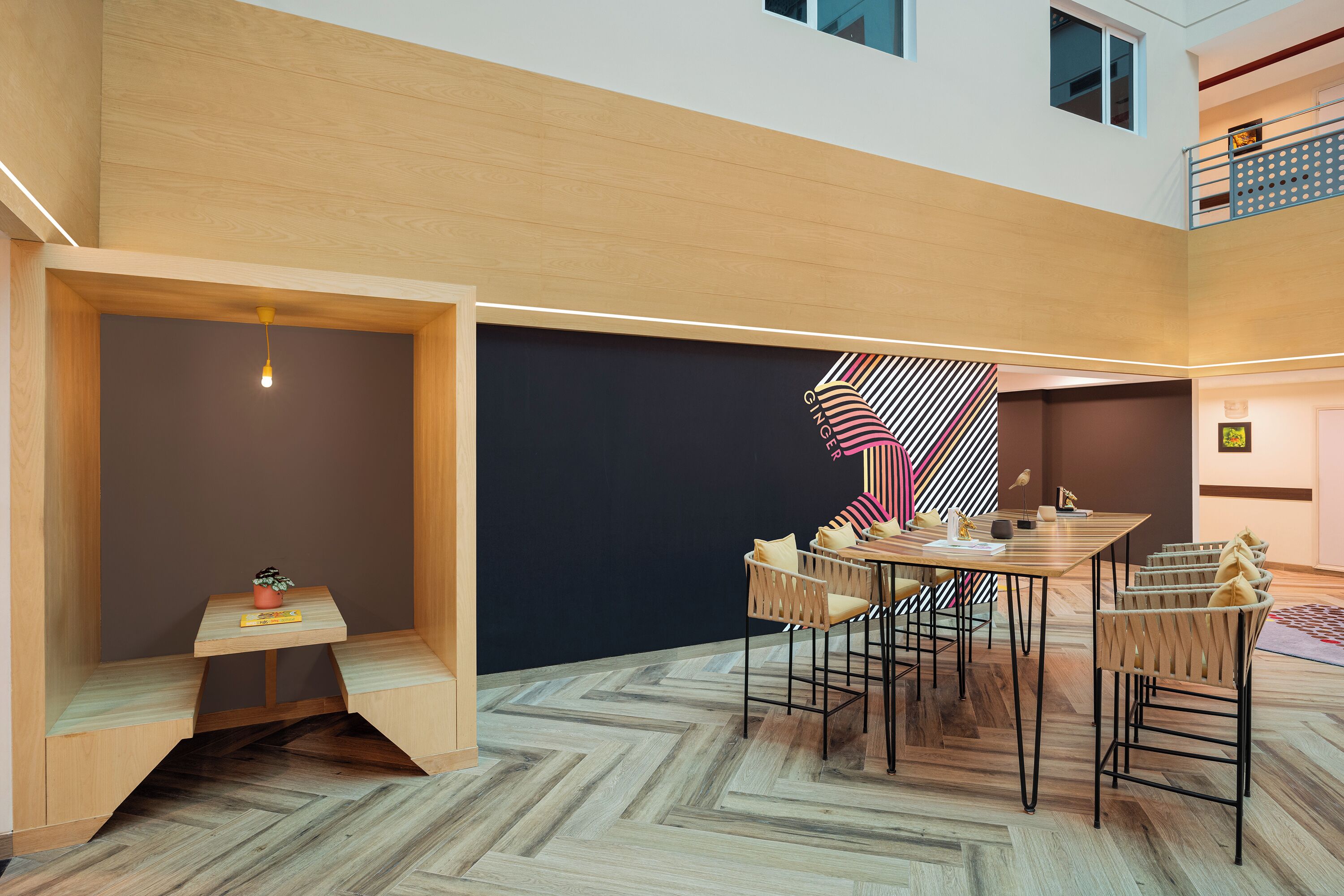 A modern interior with a dining area featuring a wooden table and chairs, a small seating area with a bench and a plant, and a herringbone-patterned floor.
