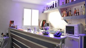 A modern bar area with a counter, shelves of liquor bottles, a microwave, and a window providing natural light. - Orsa Maggiore Hotel (Naples)