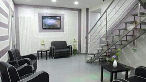 A modern waiting area with a sofa, chairs, a TV, and a staircase. - Orsa Maggiore Hotel (Naples)