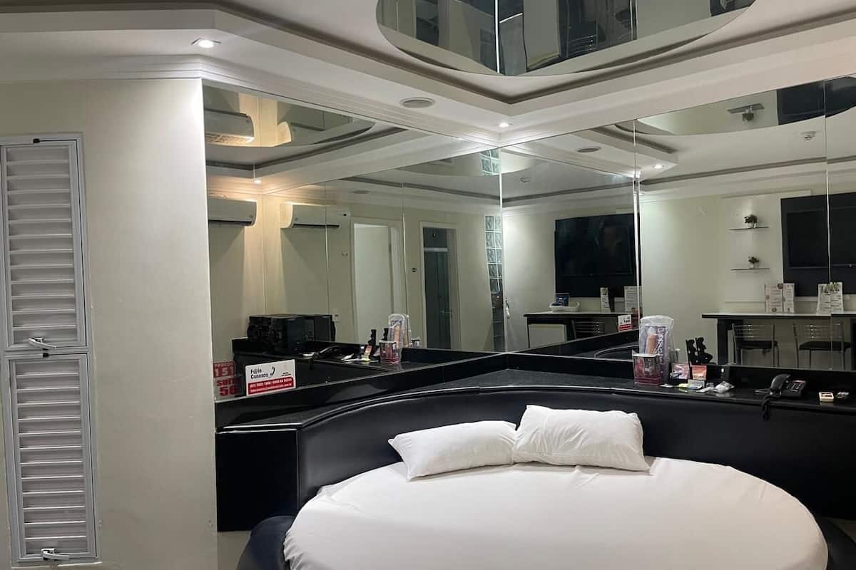 A modern hotel room with a large bed, a curved ceiling, and a large mirror reflecting the room.
