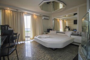 Camera d'albergo con un letto grande, una scrivania con sedie, un tavolino e un divisorio in vetro.