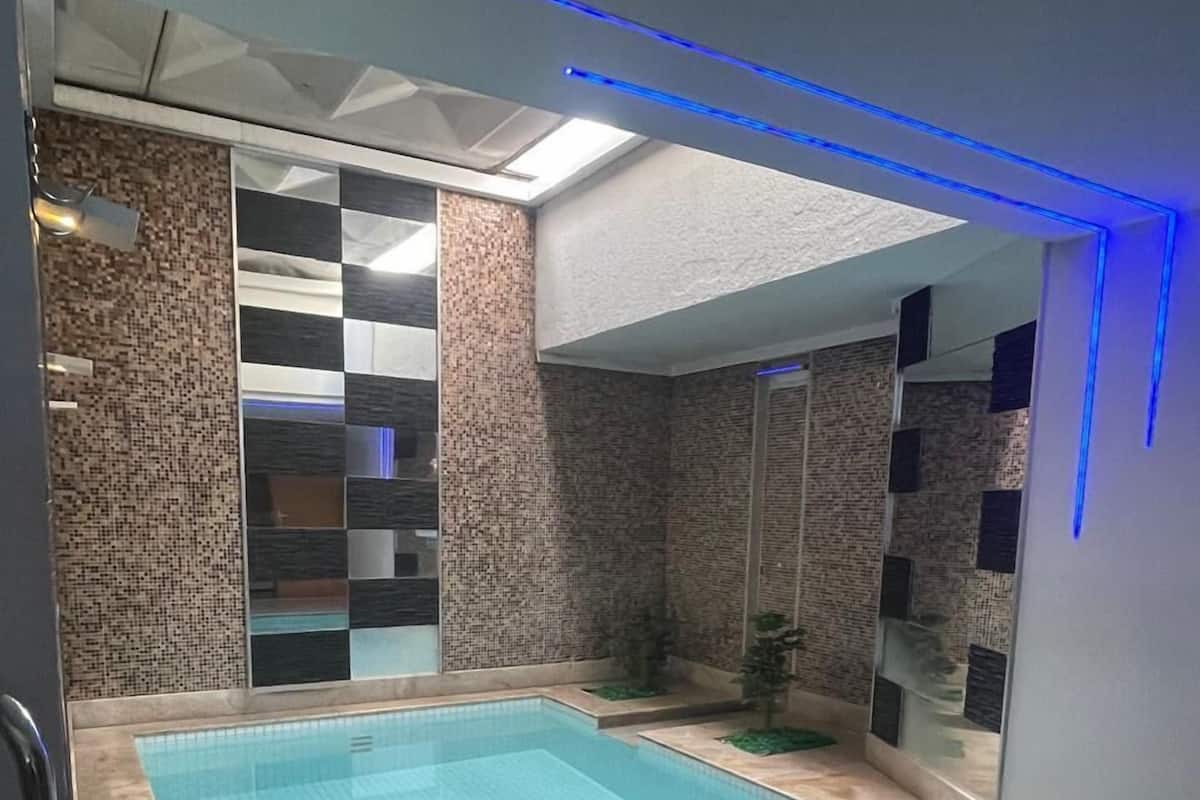 A swimming pool with a tiled floor, a glass wall, and a blue light strip.