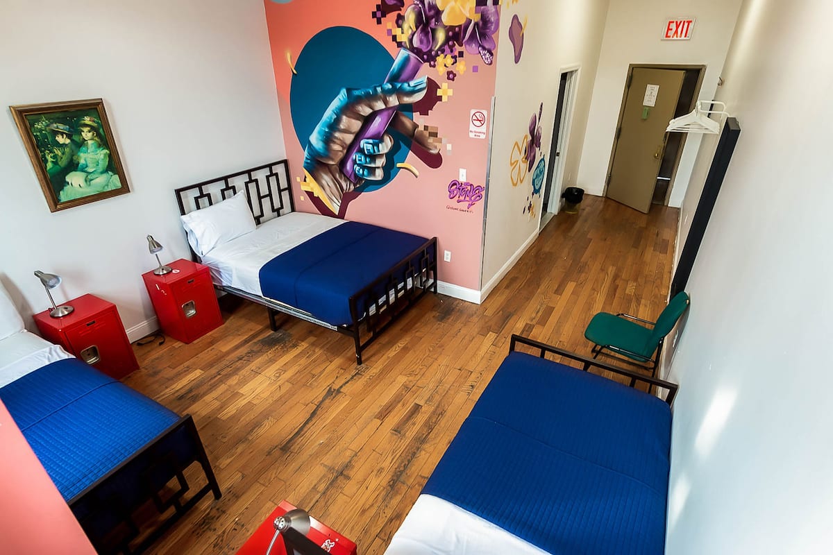 A room with a bed, a desk, and a chair. There is a door with an exit sign and a coat rack.