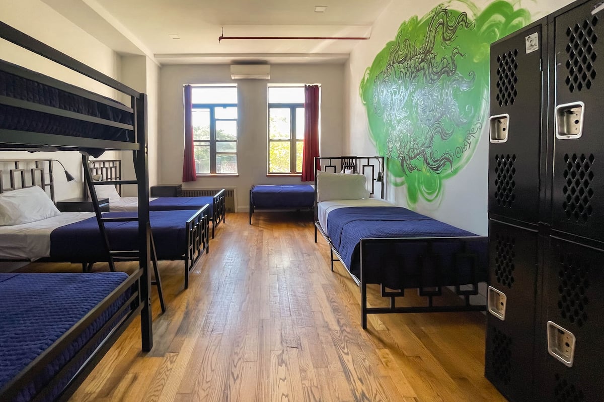 A dormitory room with bunk beds, a large window, and a green abstract mural on the wall.