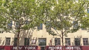 A building with "NEW YORK MOORE HOSTEL" signage, featuring a red and beige facade, multiple windows, and a tree in front. - NY Moore Hostel (Brooklyn)