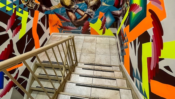 A staircase with a vibrant mural, an exit sign, and a handrail. - NY Moore Hostel (Brooklyn)