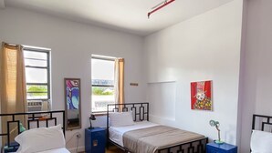 A room with three beds, a window with curtains, a painting on the wall, and a ceiling light fixture. - NY Moore Hostel (Brooklyn)
