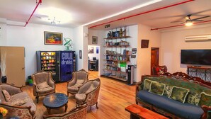 A living room with a sofa, armchairs, a coffee table, a bookshelf, a television, and a vending machine. - NY Moore Hostel (Brooklyn)