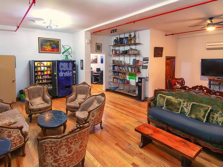 Una sala de estar con un sofá, sillones, una mesa de centro, una estantería, un televisor y una máquina expendedora.