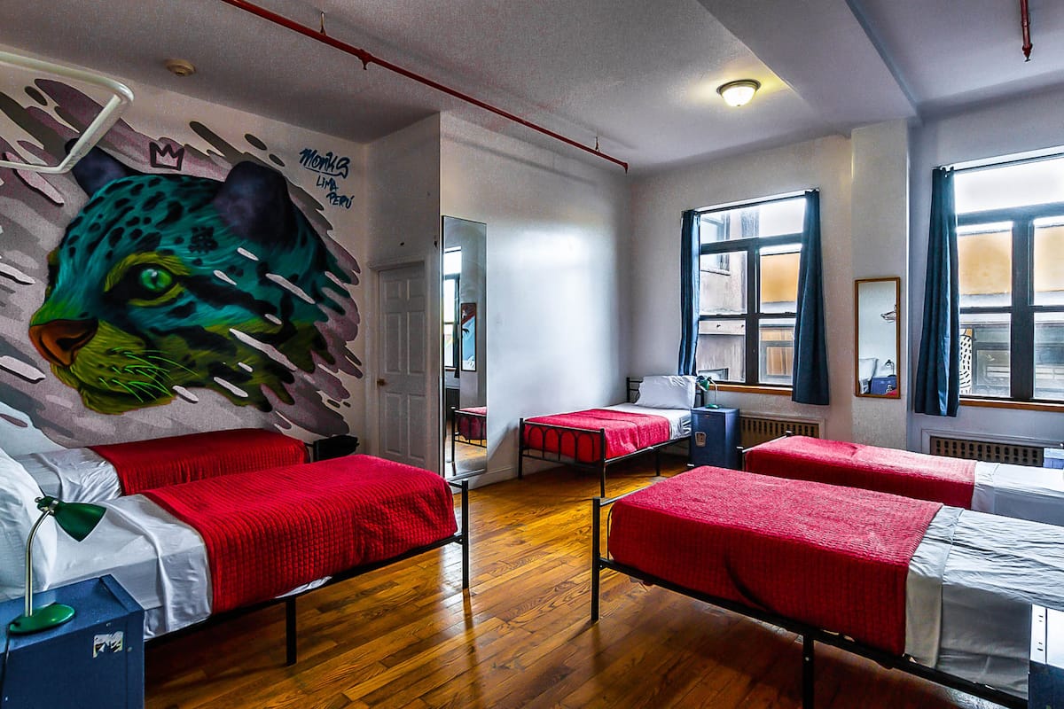 A room with three single beds, a leopard mural on the wall, and large windows with curtains.