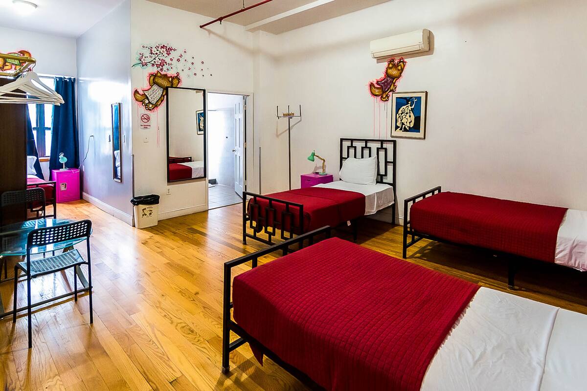 A hotel room with two single beds, a desk with a chair, a small table, a mirror, and a wardrobe.