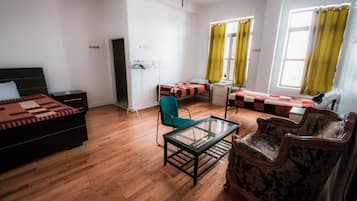 A room with a bed, a desk, a chair, and a sofa. There is a window with curtains, a radiator, and a door.
