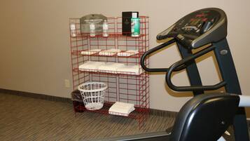 A treadmill, a red wire shelf with towels, a white laundry basket, and a water bottle.