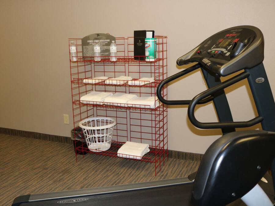 A treadmill, a red wire shelf with towels, a white laundry basket, and a water bottle.