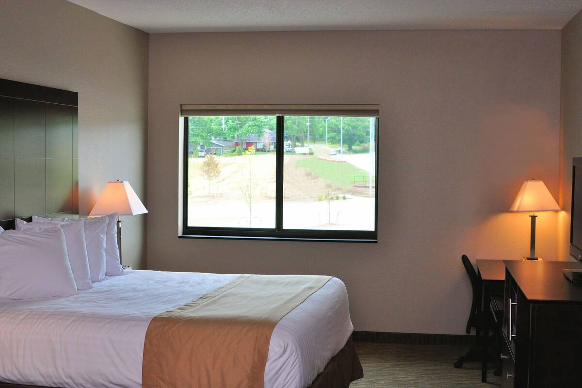 Habitación de hotel con cama, dos lámparas de noche, un escritorio con silla y un ventanal con vistas a un campo de golf.