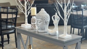 Een eettafel met decoratieve objecten, waaronder een Boeddhabeeld, een kaars en vazen.