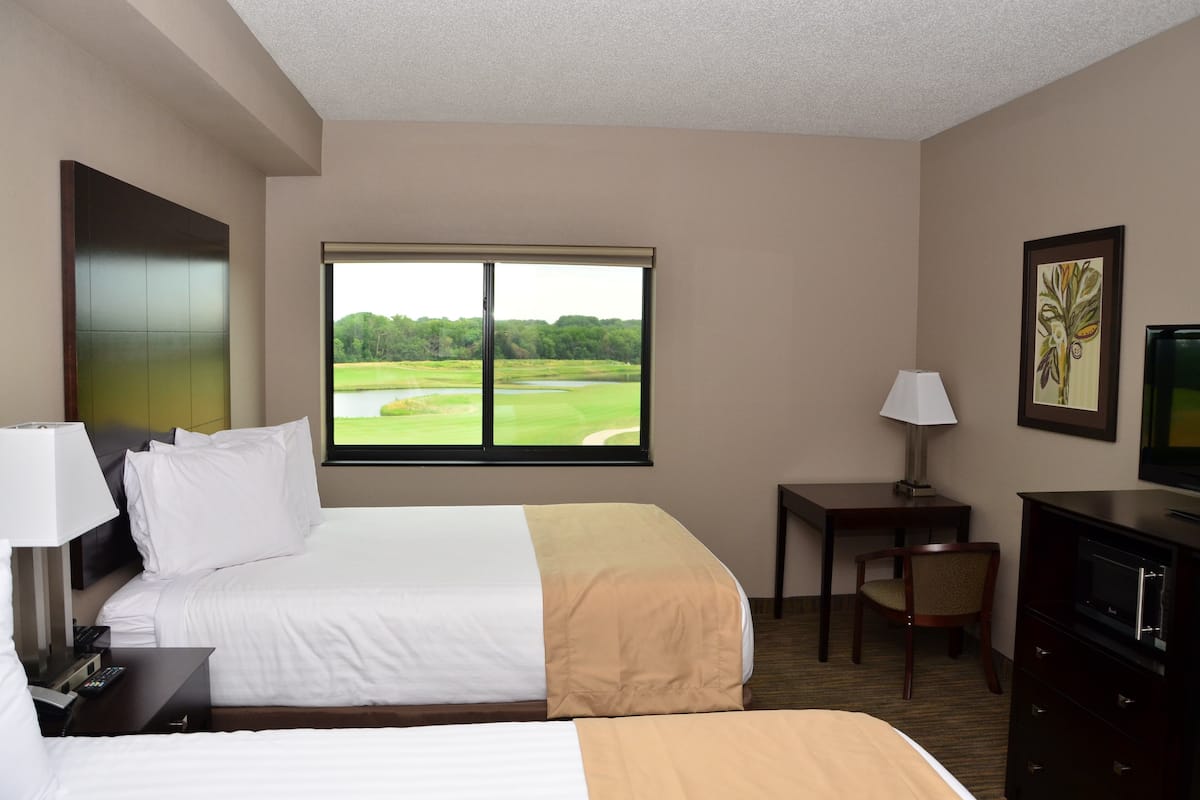 Habitación de hotel con dos camas, un escritorio, una silla, un televisor y una ventana con vista a un campo de golf.