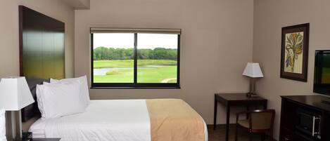A hotel room with two beds, a desk, a chair, a TV, and a window with a view of a golf course.