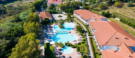 An aerial view of a resort with multiple buildings, a large swimming pool, and lush greenery.