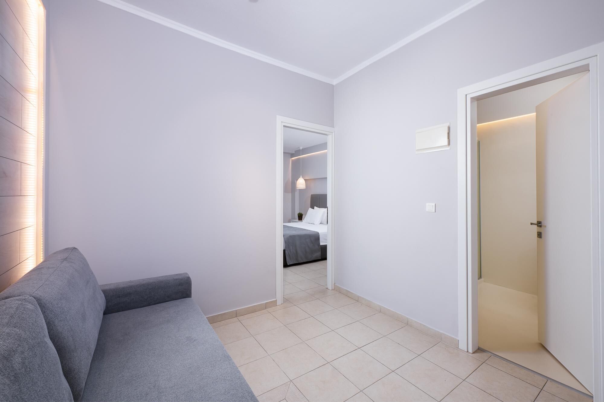 Una habitación de hotel moderna con un sofá gris, una cama con ropa blanca y una pequeña planta en maceta.