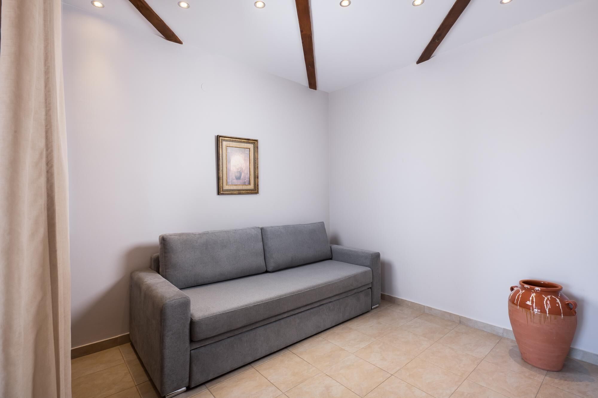 Una habitación con un sofá gris, un cuadro en la pared y una maceta de terracota en el suelo.