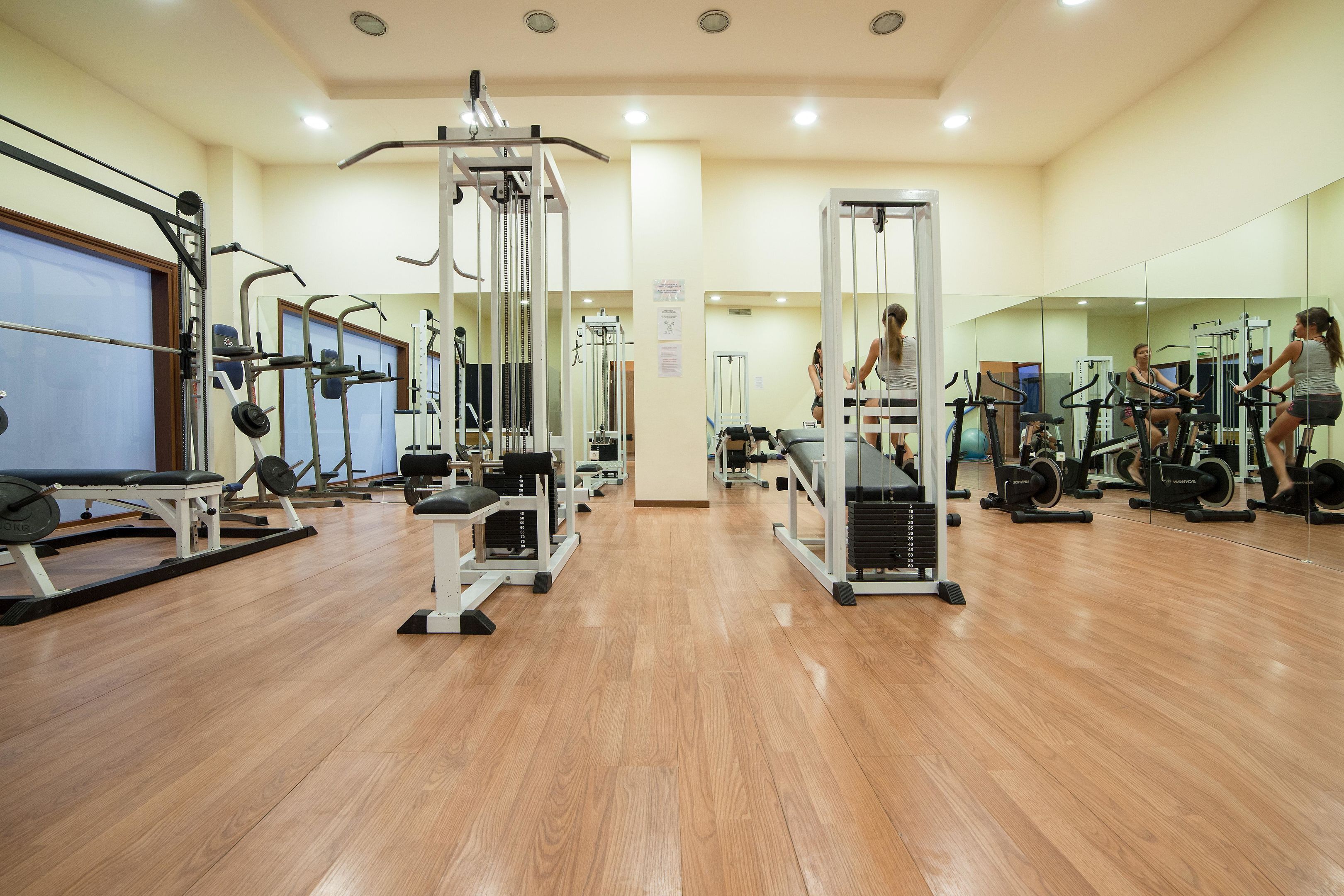 A gym with various exercise equipment, wooden flooring, and mirrors on the walls.