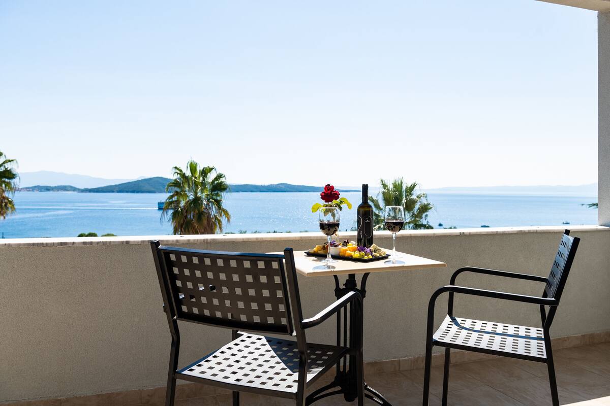 A balcony with two metal chairs, a table with a bottle of wine, glasses, and fruit.