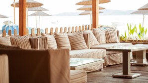 Een strandlounge met gestreepte banken, een tafel met glazen blad en rieten parasols.