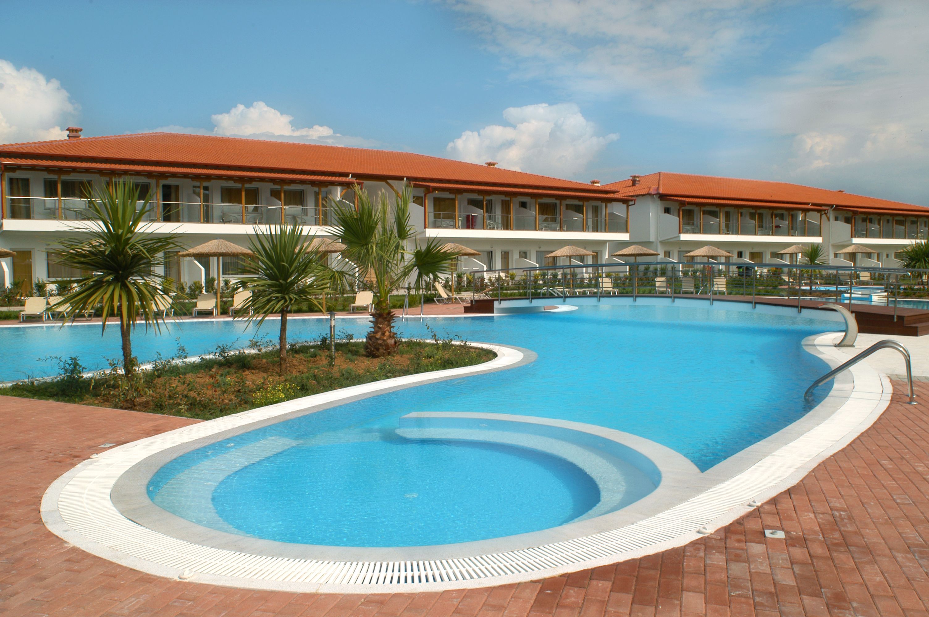 Um hotel com piscina, palmeiras e um edifício com telhado vermelho.