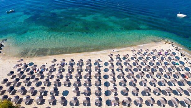 Een overzicht vanuit de lucht van een strand met rijen parasols en mensen.