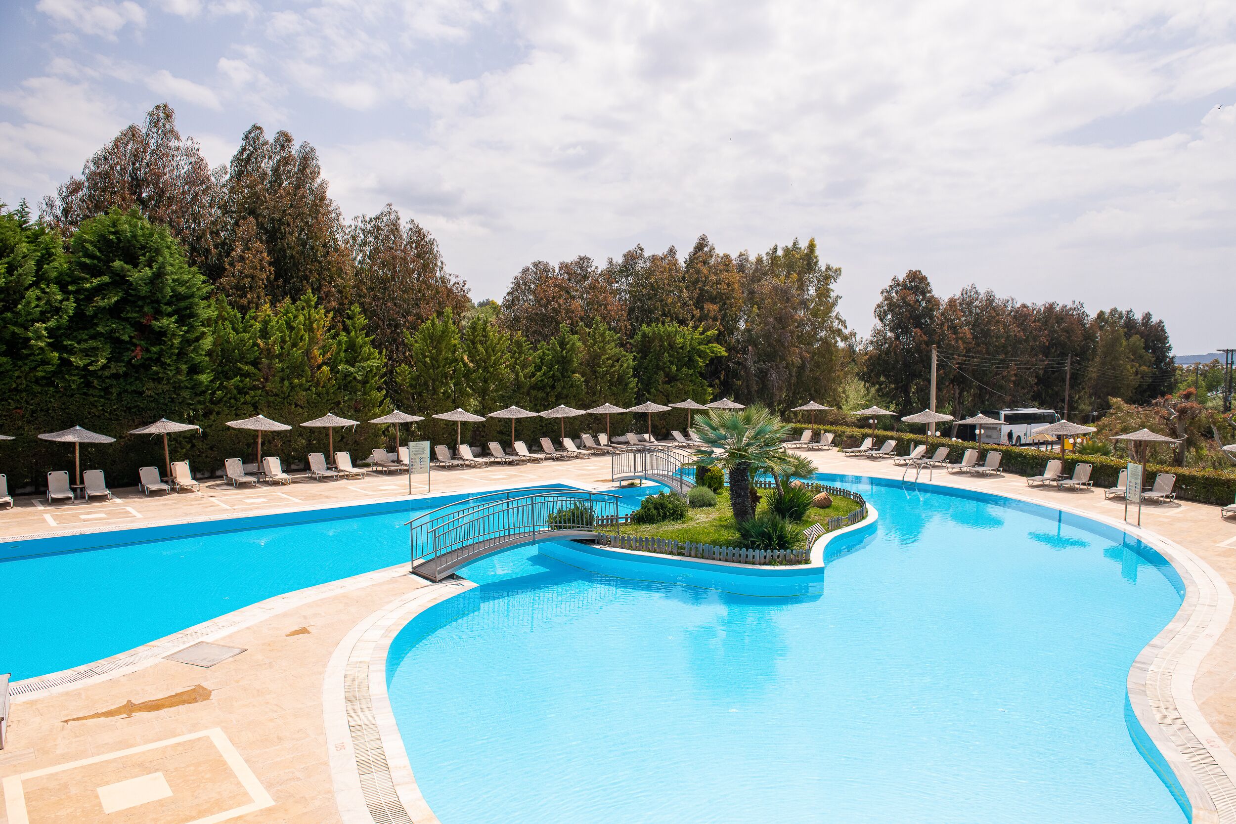 A large, curved swimming pool with lounge chairs and umbrellas, surrounded by trees.