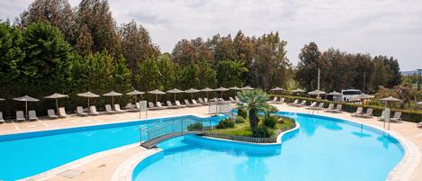 A large, curved swimming pool with lounge chairs and umbrellas, surrounded by trees.