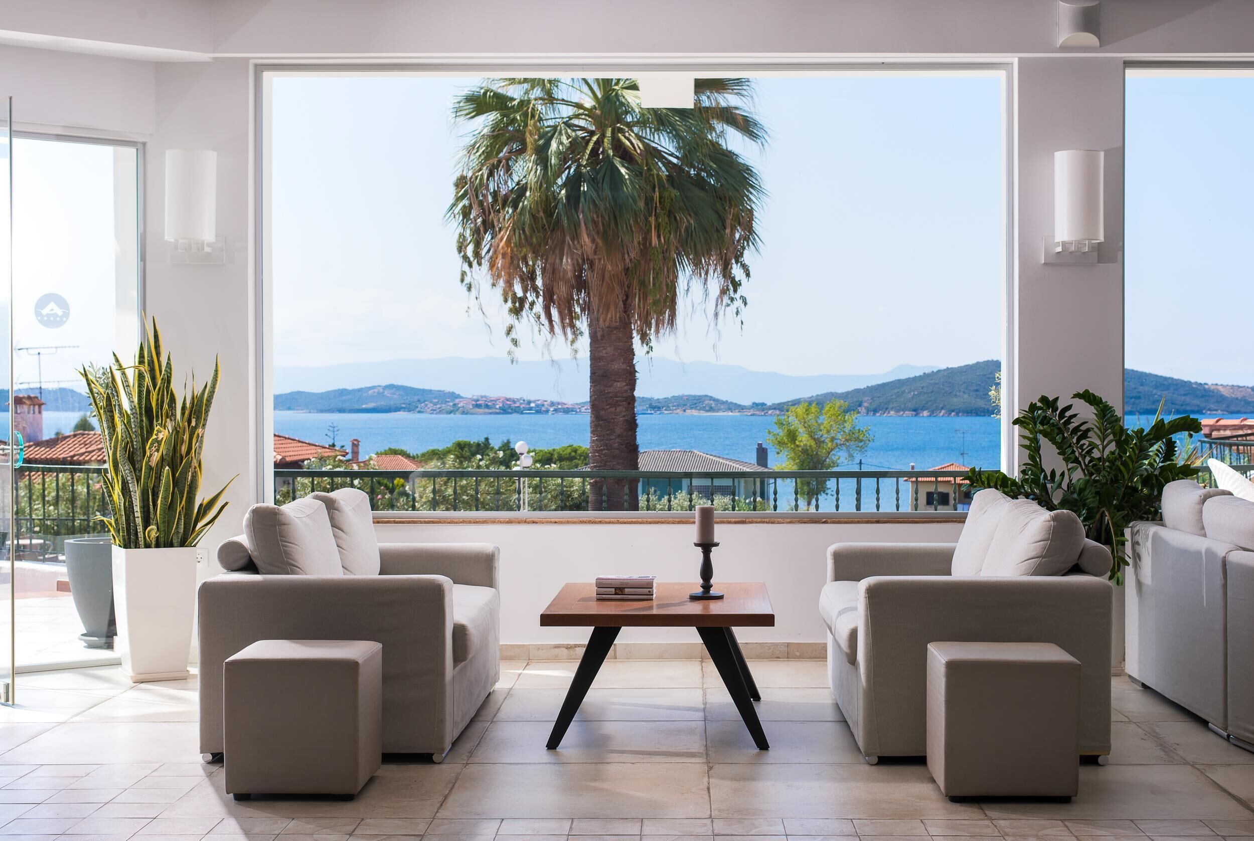Un salón moderno con un ventanal grande, dos sofás, una mesa de centro y vistas al mar y a las montañas.