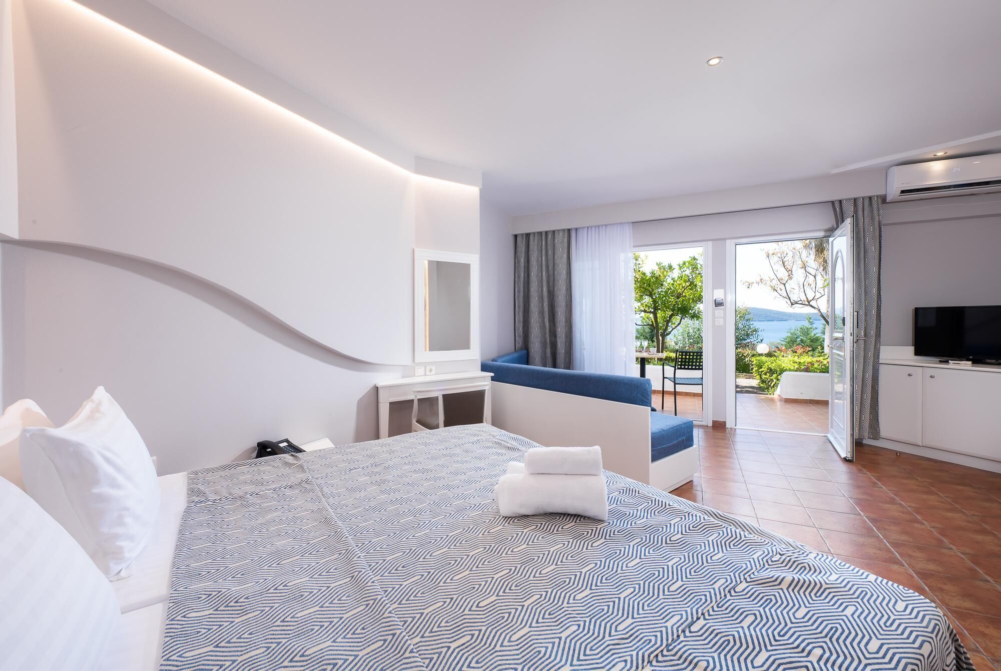 A modern hotel room with a large bed, a TV, and a balcony with a view.