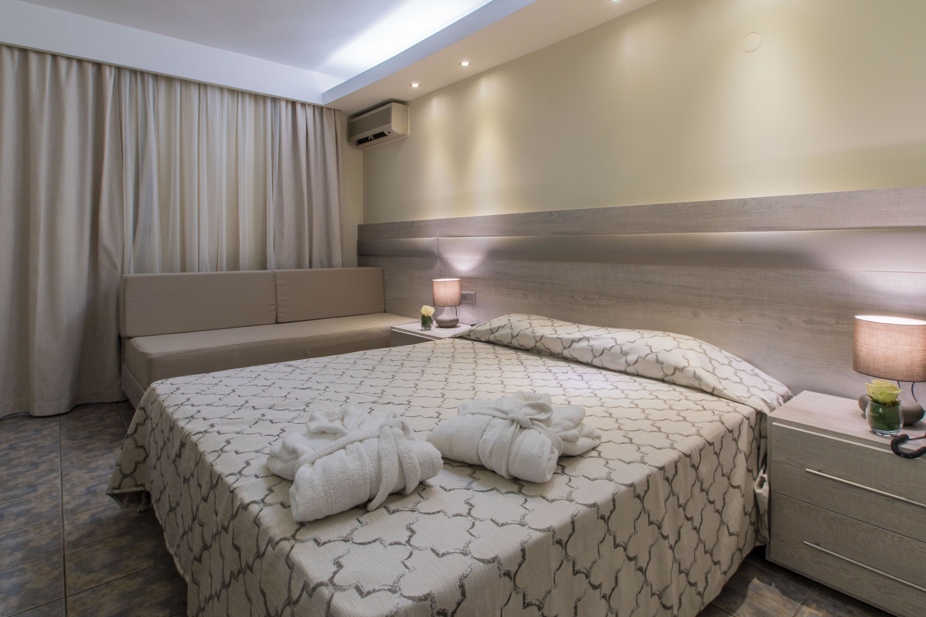 Ein Hotelzimmer mit einem großen Bett, Nachttischen, einer Lampe und einer Wand-Klimaanlage.