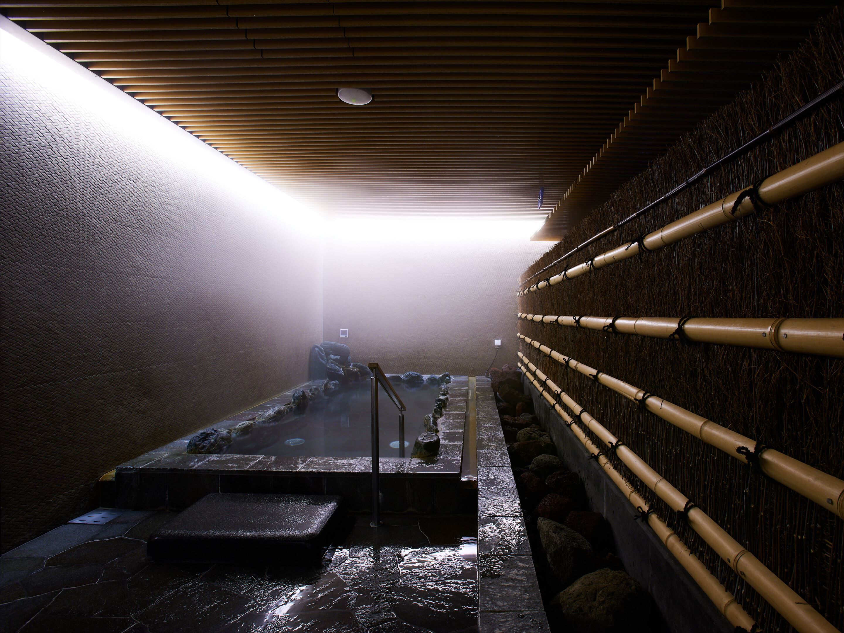 Un área de baños termales con una plataforma de piedra, pared de bambú y techo de madera.