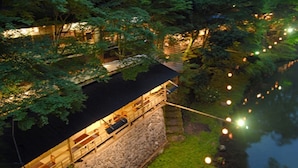 Un bâtiment situé au bord de la rivière, doté d’une façade en pierre, d’une terrasse en bois et d’un espace de détente abrité.