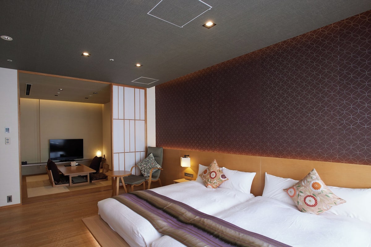 A hotel room with a large bed, a TV, a seating area, and a patterned wall.