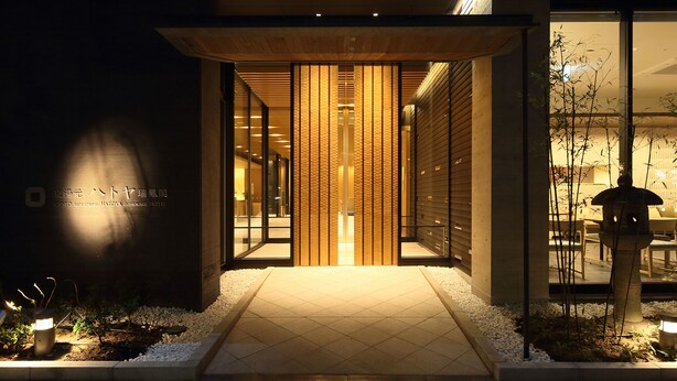 Une entrée d’hôtel moderne avec une façade en bois, des portes en verre et un chemin pavé menant à l’entrée.
